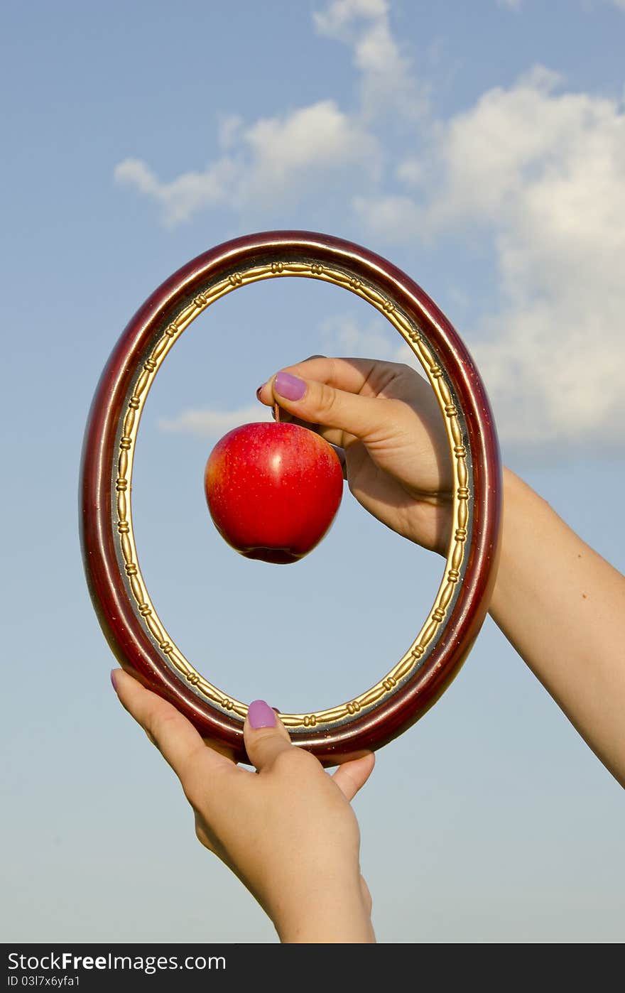 Woman hands with frame and apple on sky background