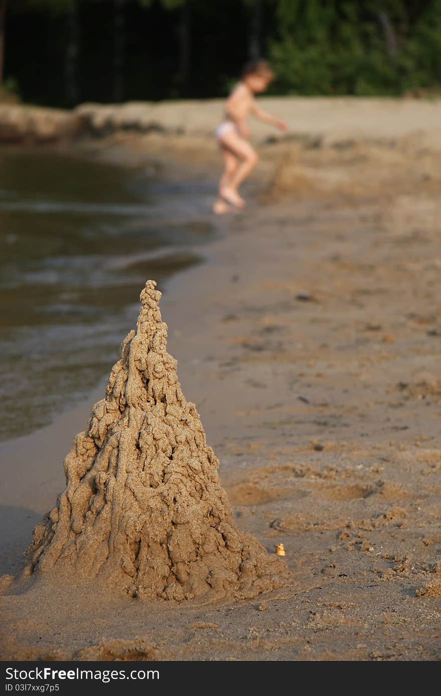 Sand castle on beach with playing child