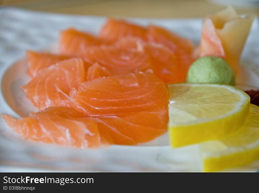 Salmon sashimi close-up with lemon, wasabi and ginger on a white plate