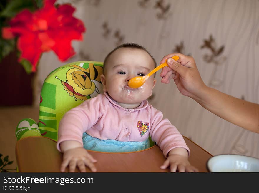 Ittle girl baby sitting for children's table and eat with a spoon feeds her mother. Ittle girl baby sitting for children's table and eat with a spoon feeds her mother