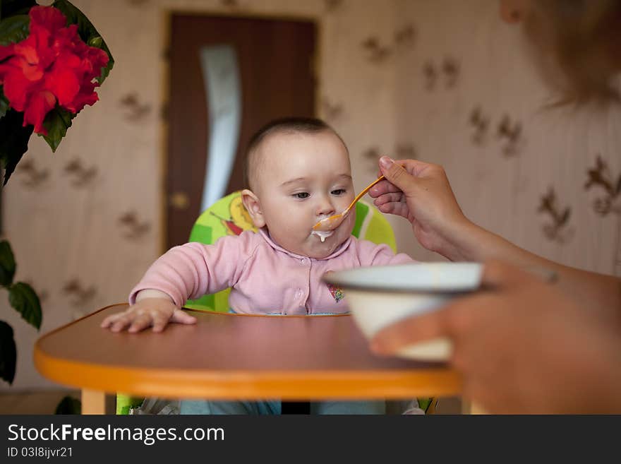 Ittle girl baby sitting for children's table and eat with a spoon feeds her mother. Ittle girl baby sitting for children's table and eat with a spoon feeds her mother