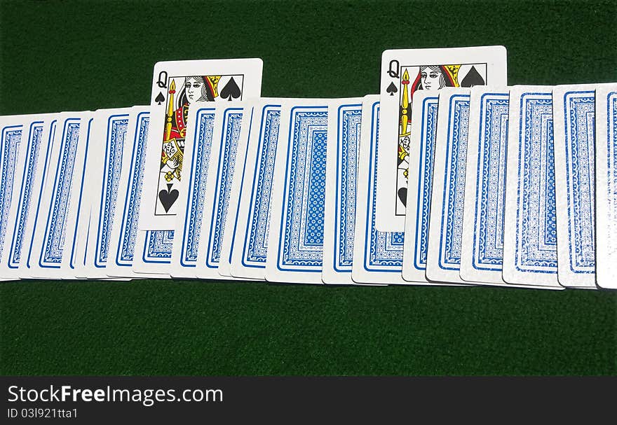 Deck of cards face-down on the green playing table with two Queens of Spades