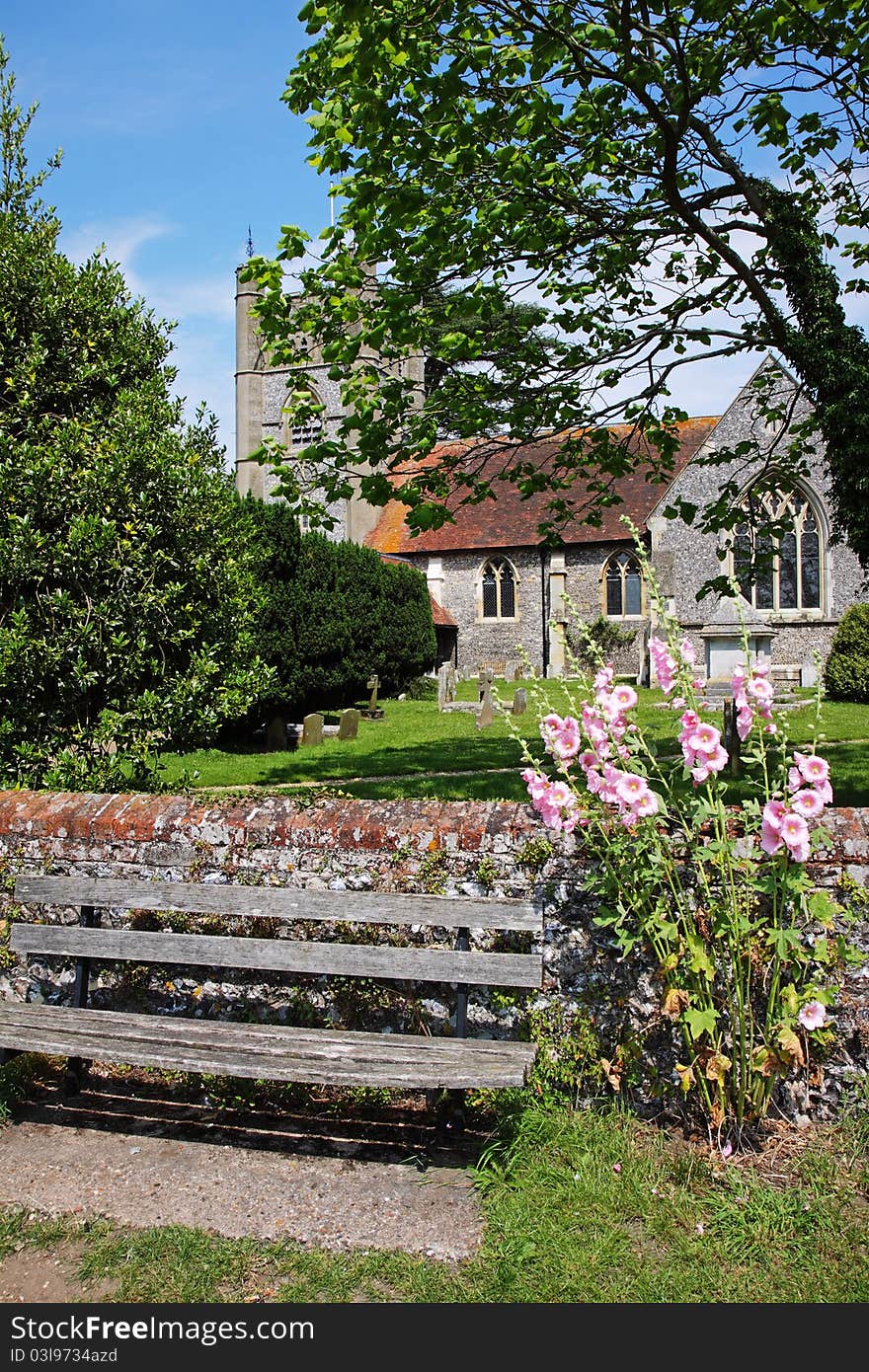 English Village Church and Tower with Hollyhocks and wooden bench in the foreground. English Village Church and Tower with Hollyhocks and wooden bench in the foreground