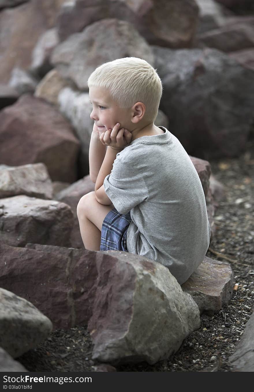 Little boy sits on rough rocks