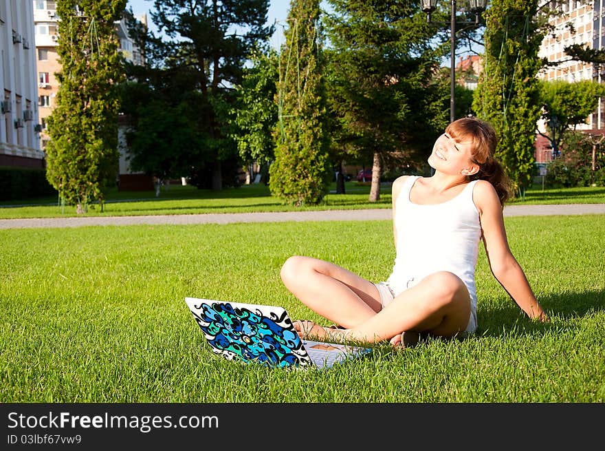 Young girl sitting in the park with your laptop, green grass backgrounf