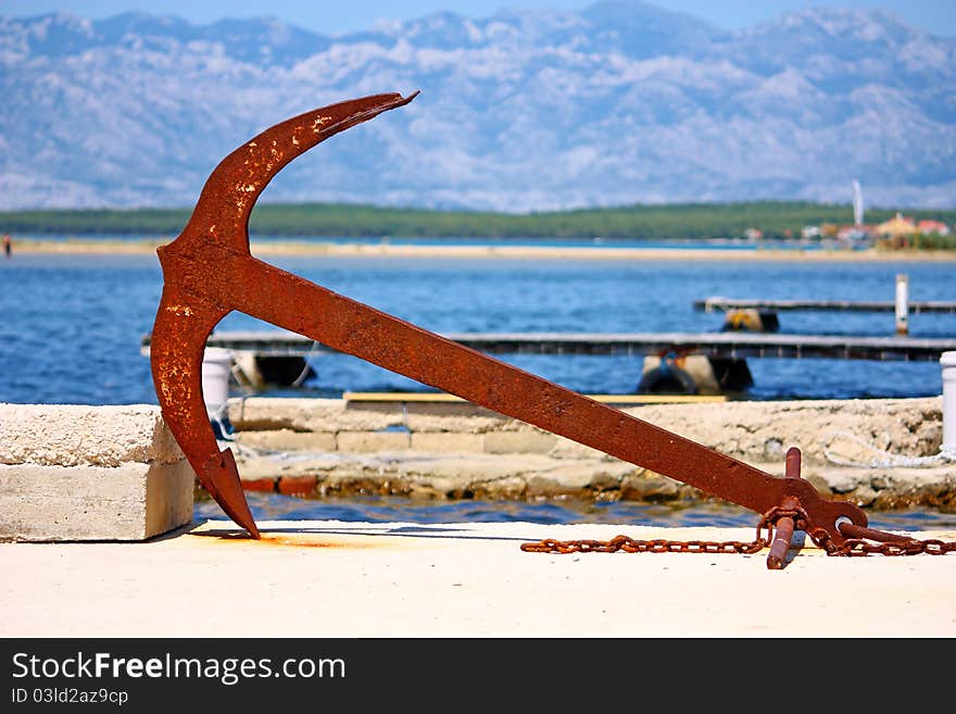 An old rusty anchor on the ground in port. An old rusty anchor on the ground in port