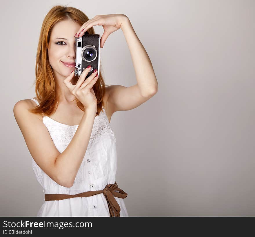 Redhead girl in white dress with vintage camera. Studio shot.