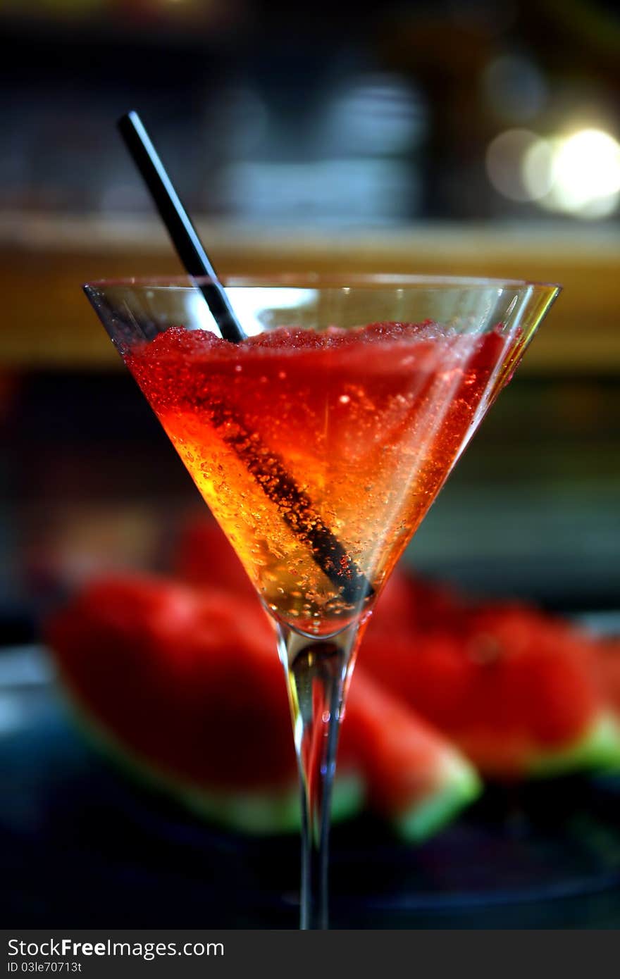 Goblet with cold coloured drink and background with slices of watermelon. Goblet with cold coloured drink and background with slices of watermelon