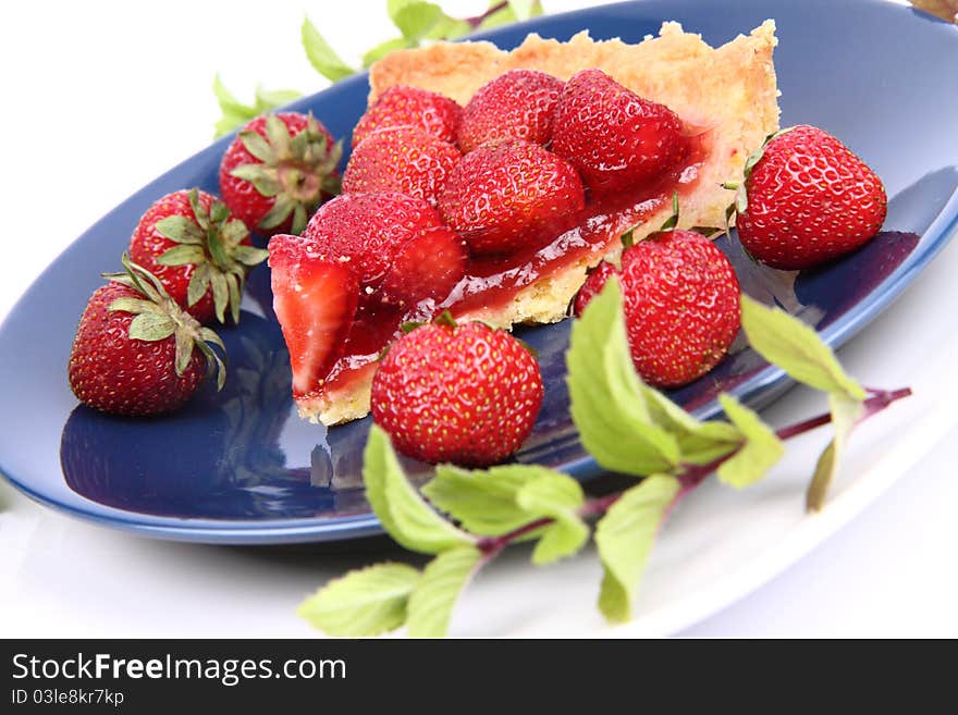 Piece of Strawberry Tart on white plate decorated with strawberries and mint twigs