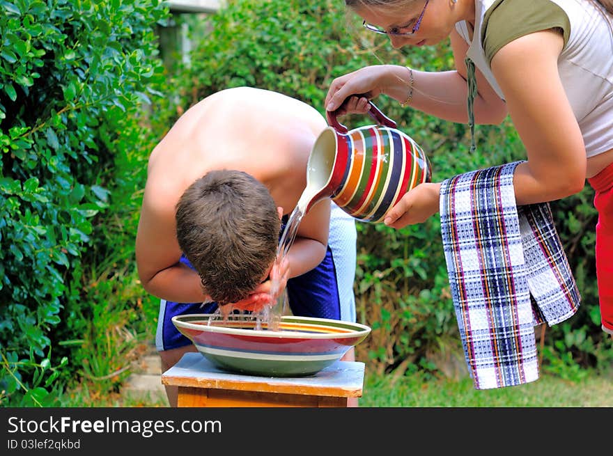 A boy washes over a bowl, and mom poured him water from a pitcher. A boy washes over a bowl, and mom poured him water from a pitcher