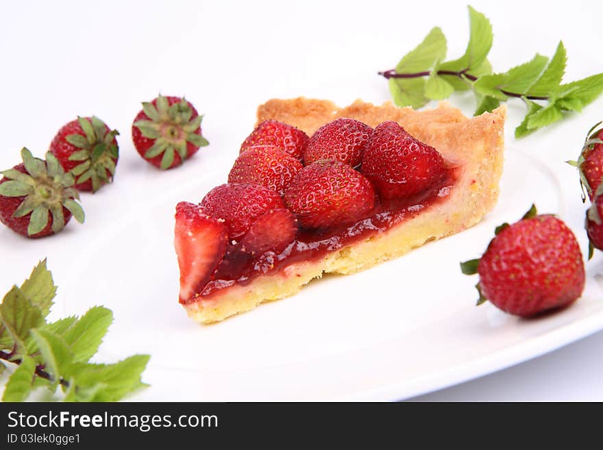 Piece of Strawberry Tart on white plate decorated with strawberries and mint twigs