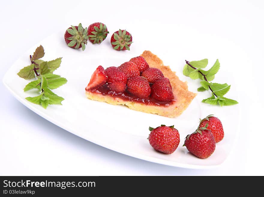 Piece of Strawberry Tart on white plate decorated with strawberries and mint twigs