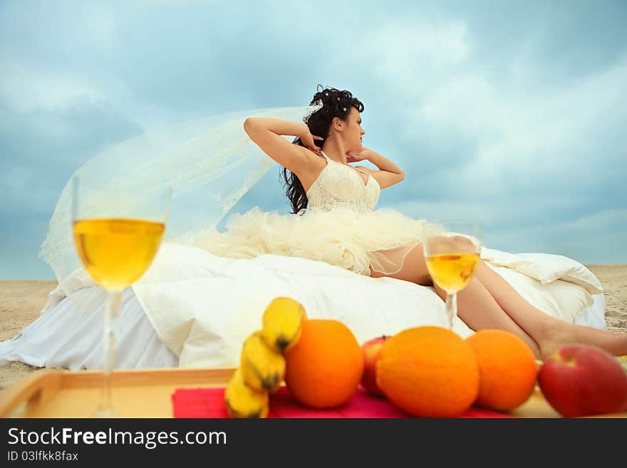 Young bride in bed at the coastline against cloudy sky