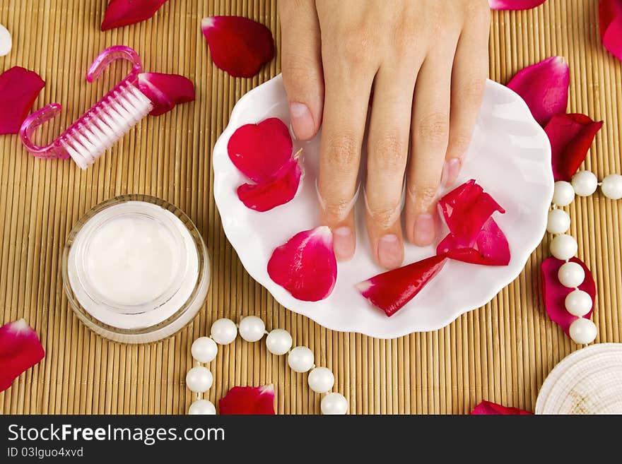 Close-up of girl's hand dropped into a saucer of water near a lot of rose petals. Spa services. Close-up of girl's hand dropped into a saucer of water near a lot of rose petals. Spa services