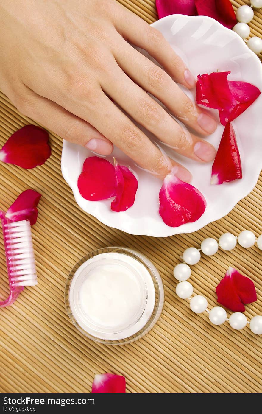 Close-up of girl's hand dropped into a saucer of water near a lot of rose petals. Spa services. Close-up of girl's hand dropped into a saucer of water near a lot of rose petals. Spa services