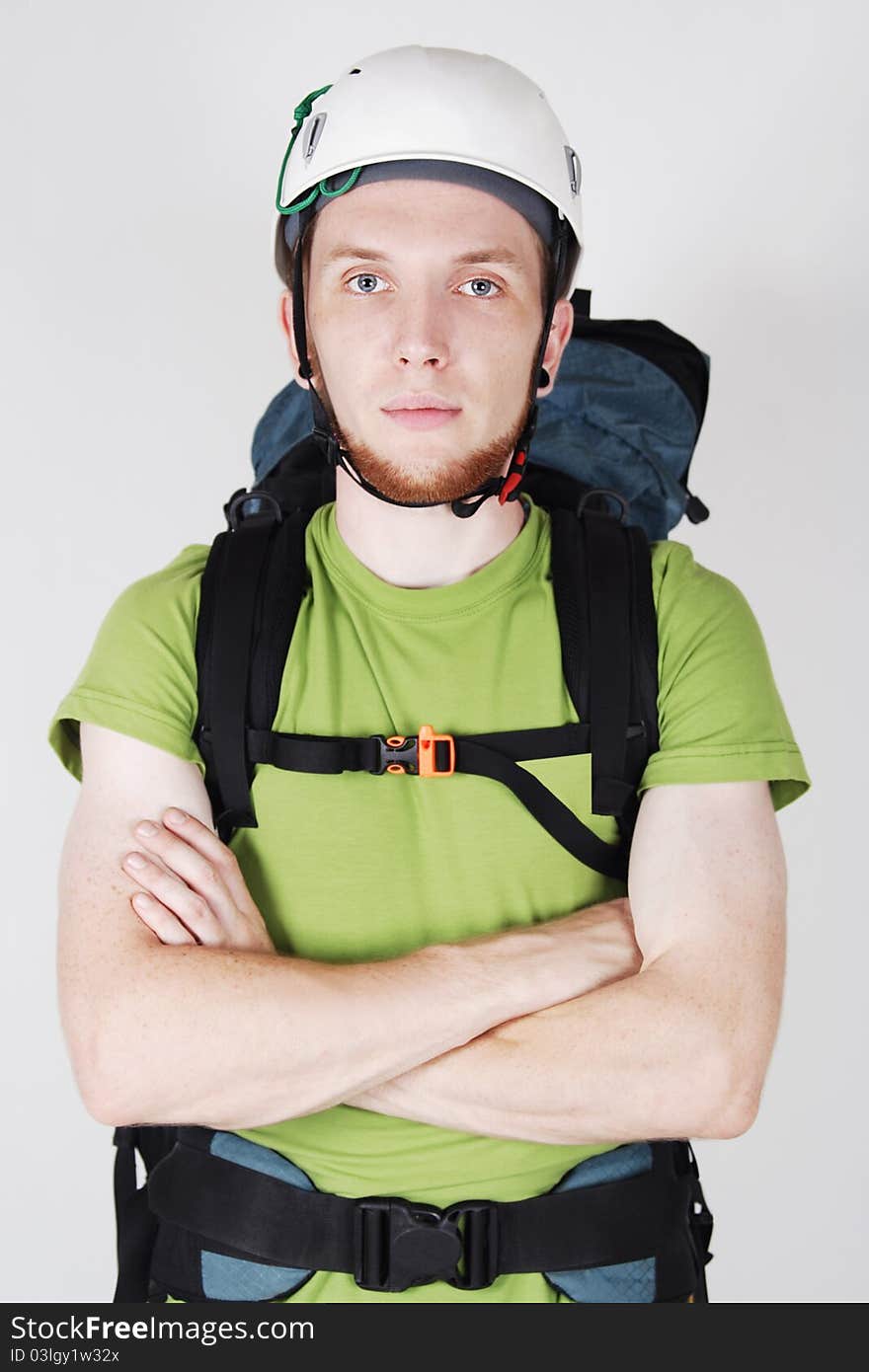 Mountain tourist in helmet and with big backpack standing with crossed hands