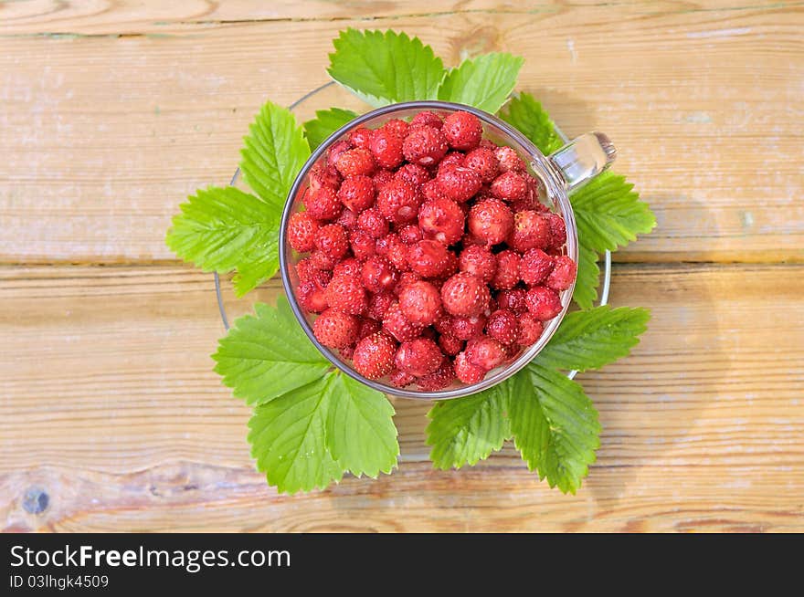 Strawberries. Wild strawberry. Strawberries in a glass bowl on a wooden table. The strawberries and green leaves.