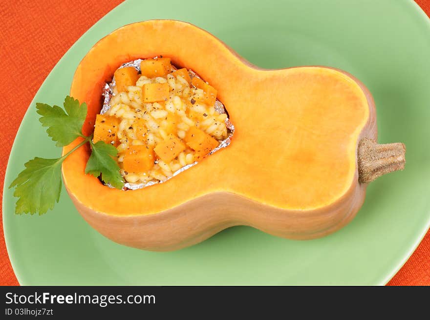 Half pumpkin filled with pumpkin risotto served on a green plate