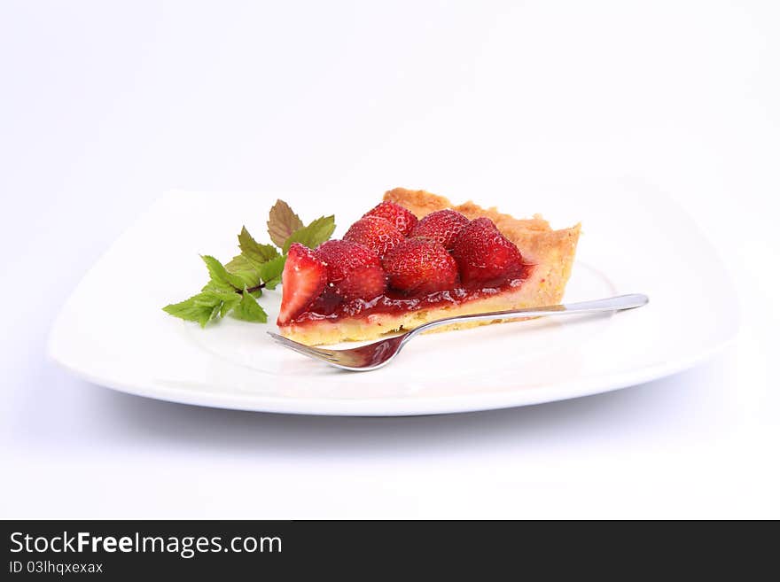 Piece of Strawberry Tart on white plate decorated with mint twig