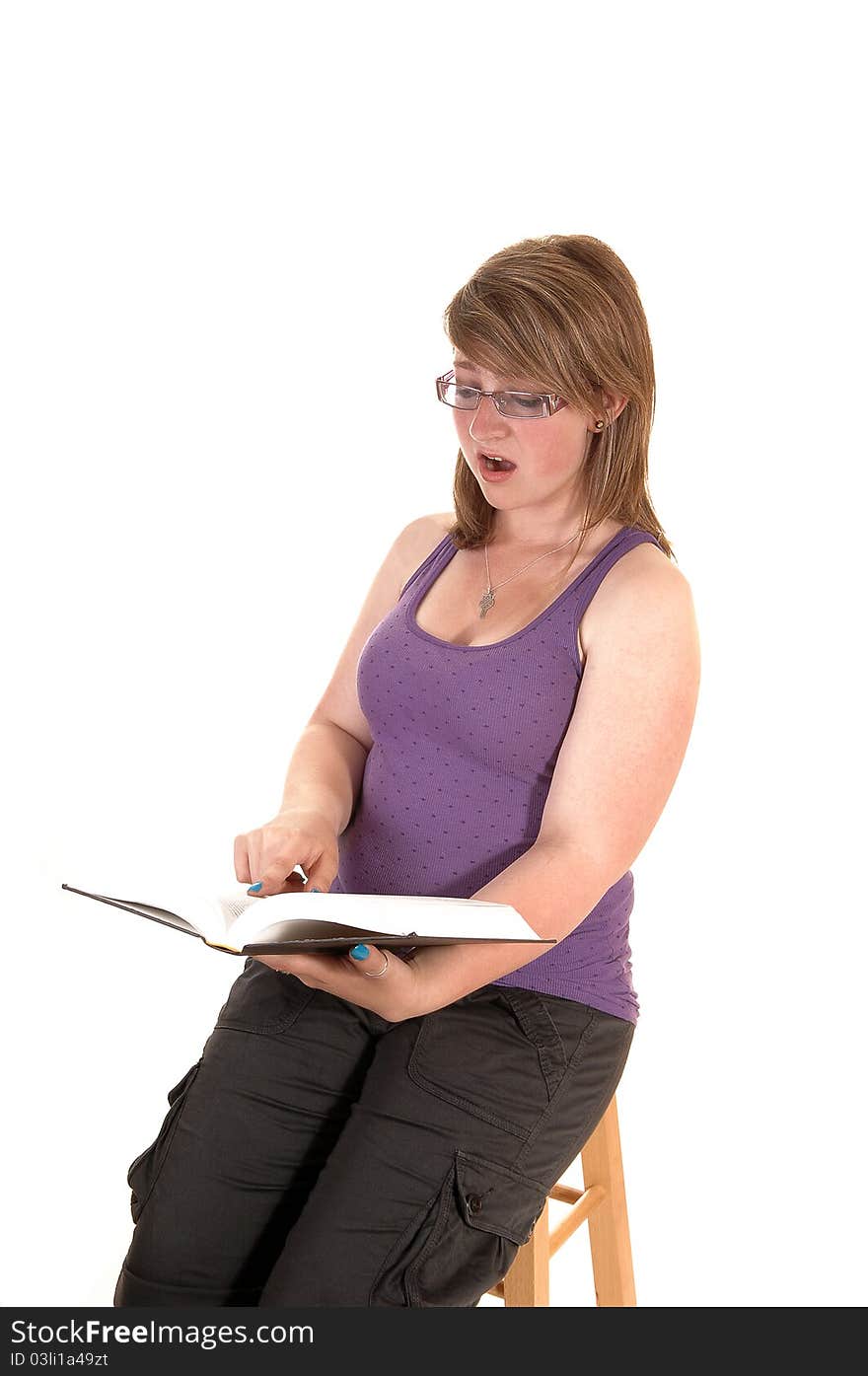 An pretty teenage girl is very surprised what she is reading in the book she is holding in her hands, sitting on a chair, over white. An pretty teenage girl is very surprised what she is reading in the book she is holding in her hands, sitting on a chair, over white.