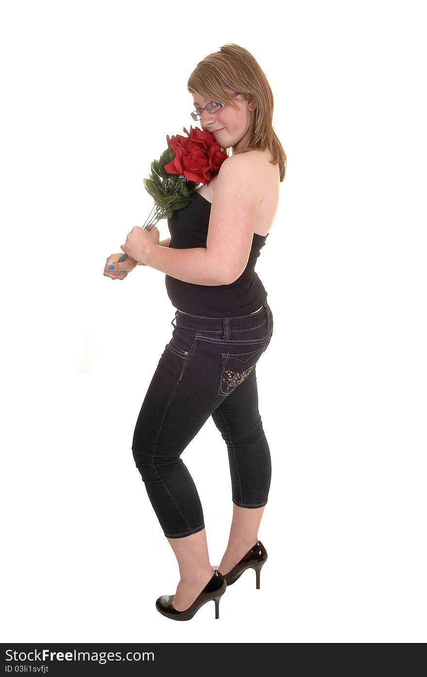 A pretty teenager standing in profile for white background, holding a bunch of red roses in her hand, in jeans and high heels. A pretty teenager standing in profile for white background, holding a bunch of red roses in her hand, in jeans and high heels.