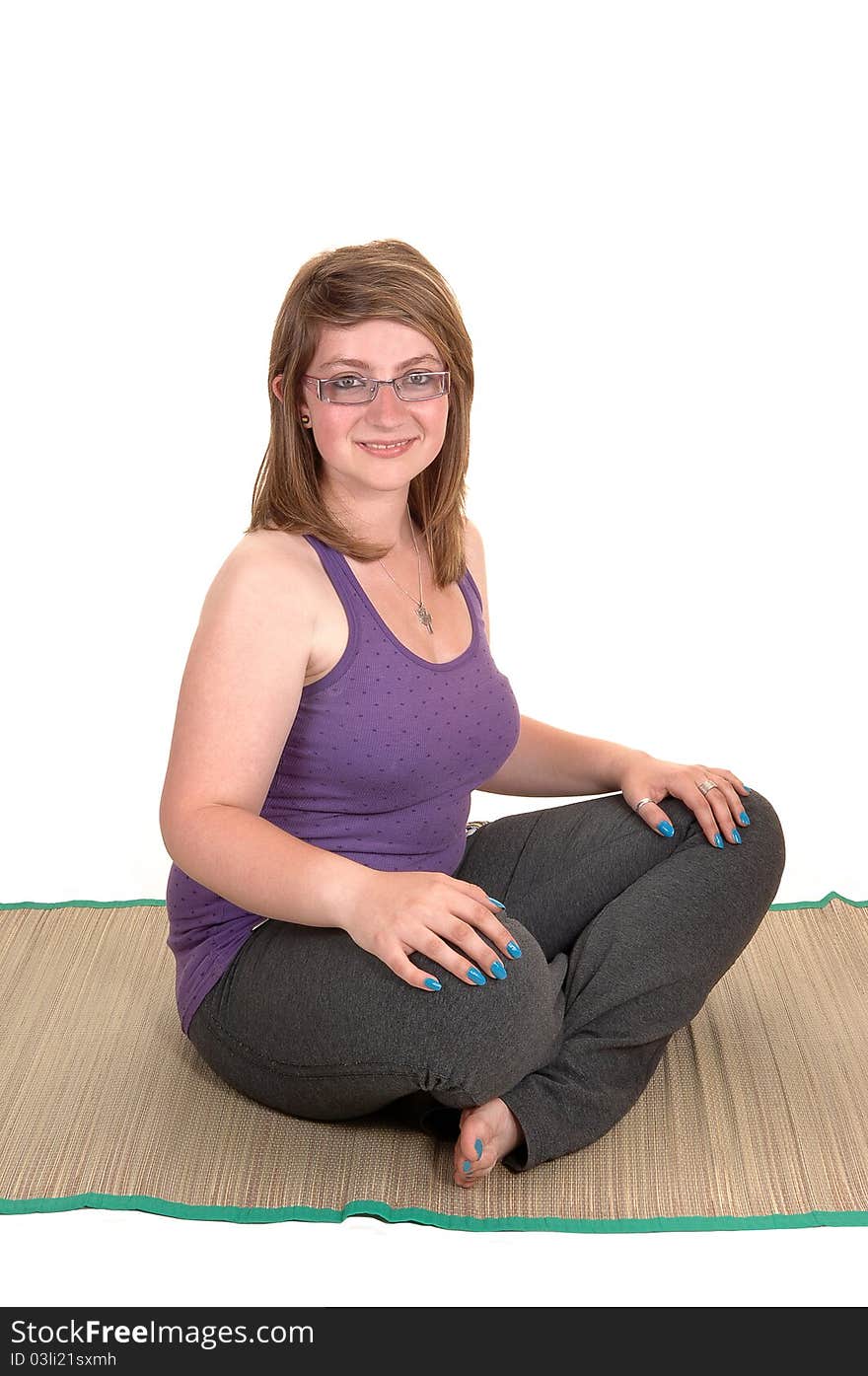 A young pretty teenager sitting on a yoga matt on the floor, with her legs grossed, smiling into the camera for white background. A young pretty teenager sitting on a yoga matt on the floor, with her legs grossed, smiling into the camera for white background.