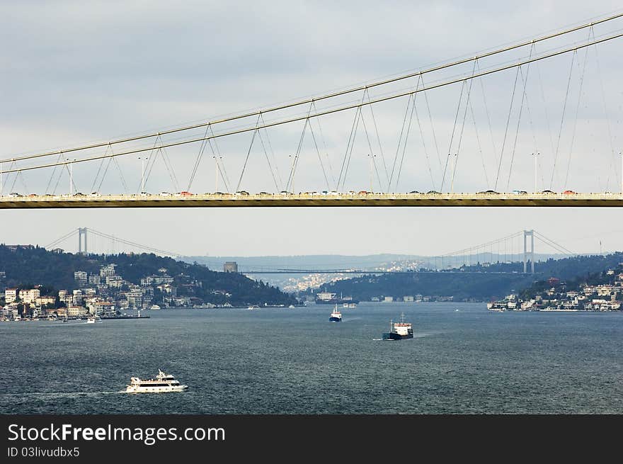 The Bosporus Bridge whcih spans the Bosphorous. Industrial Ship passing through straits of Bosphorus. Bosporus Bridge behind, Rumeli Fortress, Fatih Sultan Mehmet Bridge . Partial cloud and local sun light. The Bosporus Bridge whcih spans the Bosphorous. Industrial Ship passing through straits of Bosphorus. Bosporus Bridge behind, Rumeli Fortress, Fatih Sultan Mehmet Bridge . Partial cloud and local sun light