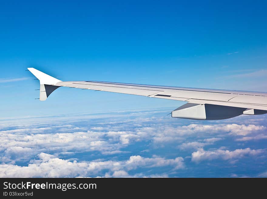 Wing of the plane with blue sky and smooth clouds