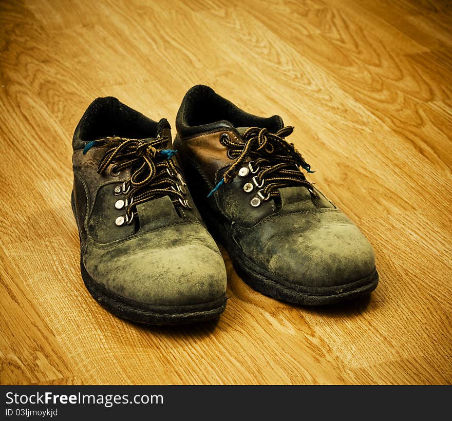 Pair of old used trekking boots on the wood background. Pair of old used trekking boots on the wood background