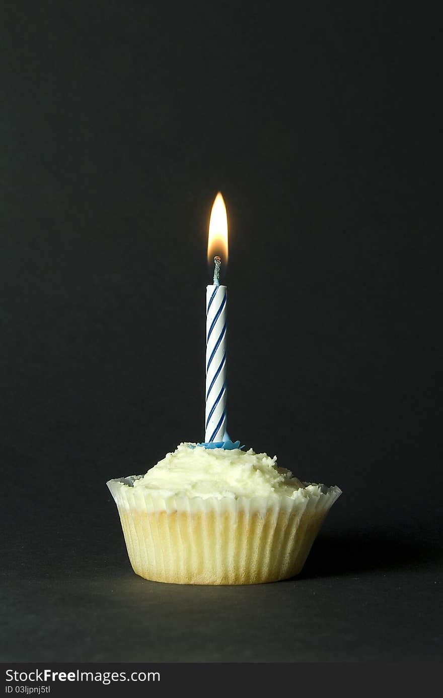 Iced cupcake with single blue birthday candle on black background. Iced cupcake with single blue birthday candle on black background