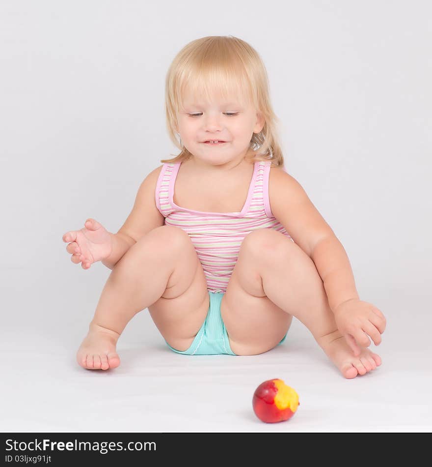 Adorable girl eat red fresh peach sitting on white