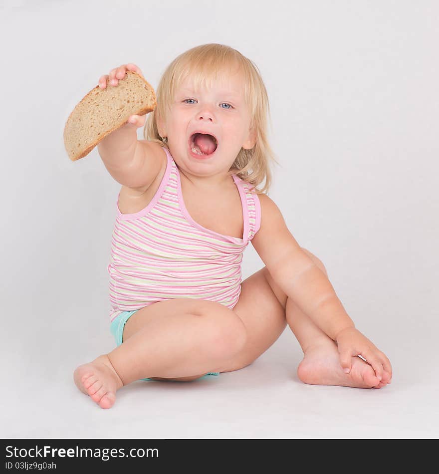 Adorable toddler girl eat rye bread sitting on white. Adorable toddler girl eat rye bread sitting on white