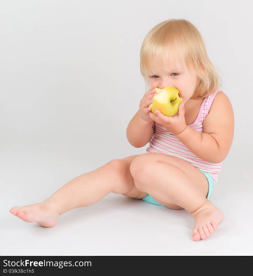 Adorable toddler girl eat green fresh apple sitting on white. Adorable toddler girl eat green fresh apple sitting on white