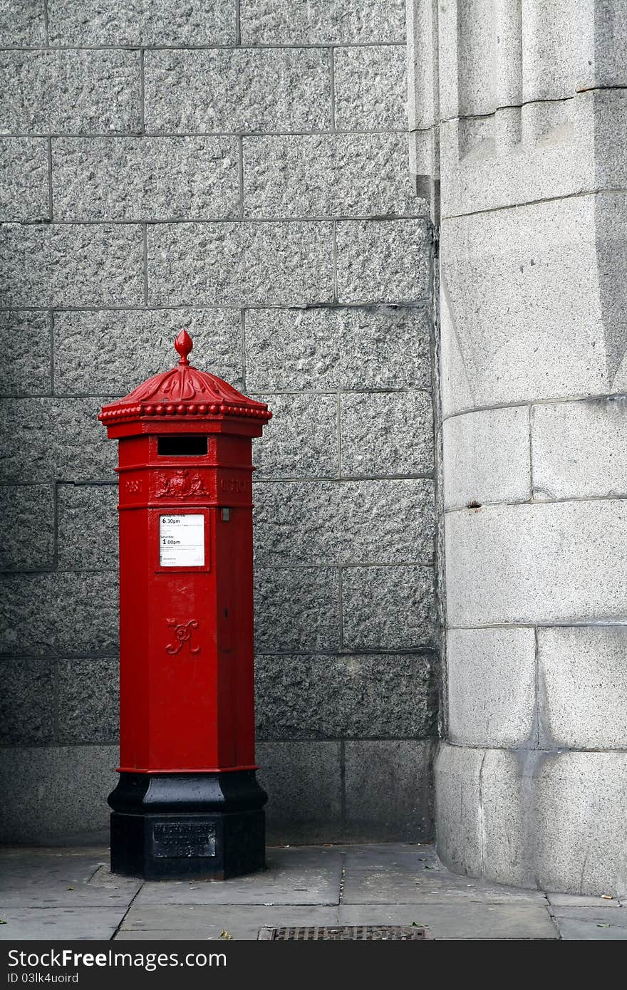 An old red free standing post box,with stone wall behind.