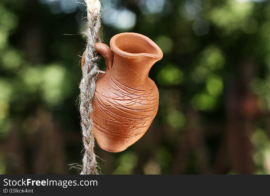 An earthen pot hanging on a rope on a background of green leaves. An earthen pot hanging on a rope on a background of green leaves