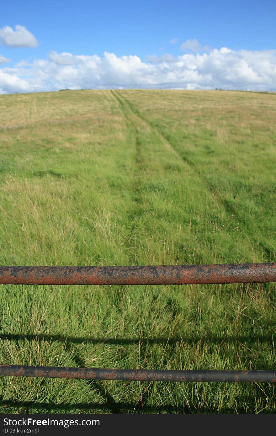 Gate and track across the fields under a blue sky, with interesting dramatic clouds. Taken in the Warwickshire countryside, England