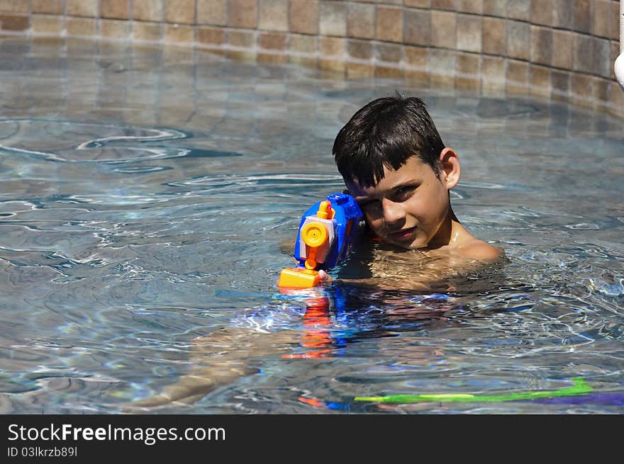 A 9 year old boy playing in the pool with a water gun. A 9 year old boy playing in the pool with a water gun.