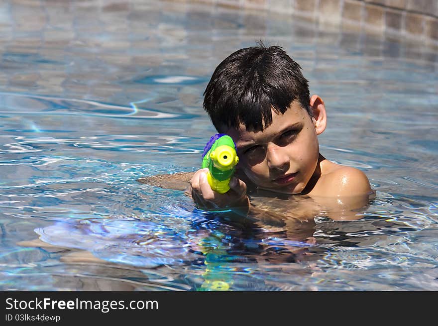 A 9 year old boy playing in the pool with a water gun. A 9 year old boy playing in the pool with a water gun.