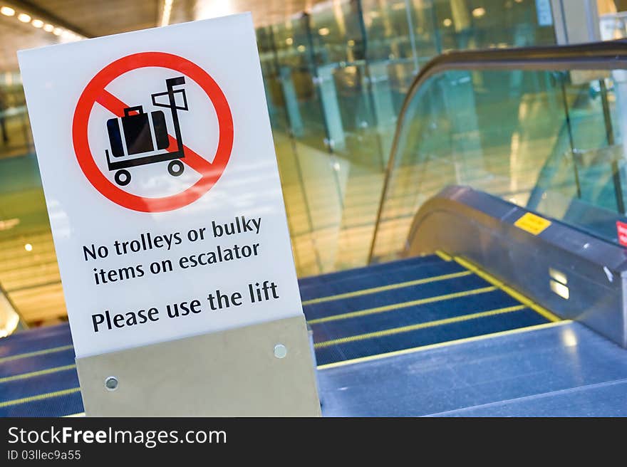 A warning signboard before the escalator at the airport, advising tourists with trolleys or bulky items to use the lift instead. A warning signboard before the escalator at the airport, advising tourists with trolleys or bulky items to use the lift instead.