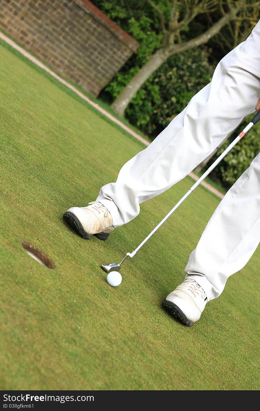 Image of a golfer standing on the green in bright sunlight putting the ball