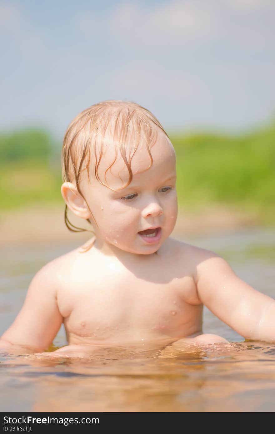 Adorable baby sit in river and play with sand and wood branch