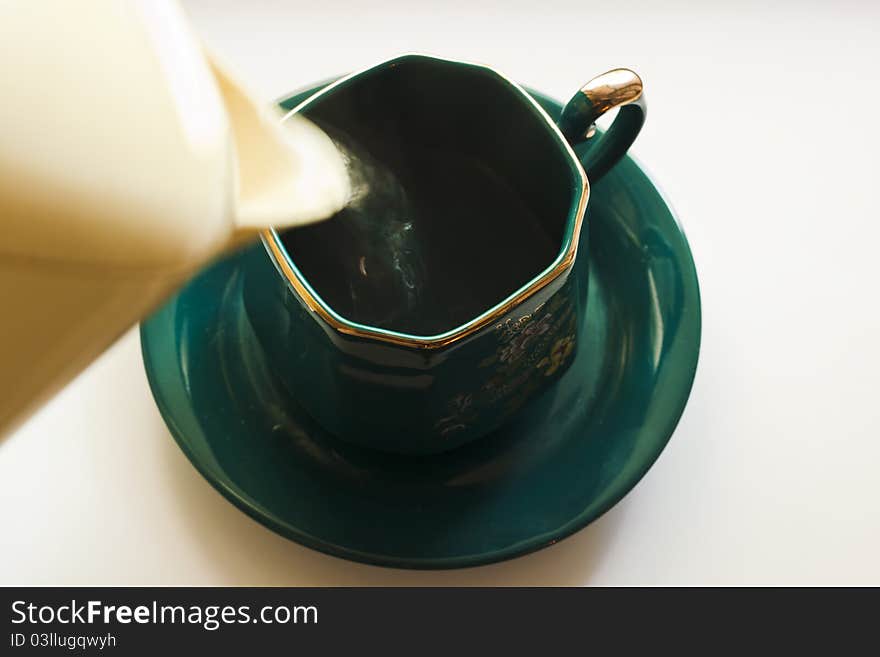 Boiling water is poured from a teapot into a green cup on a saucer