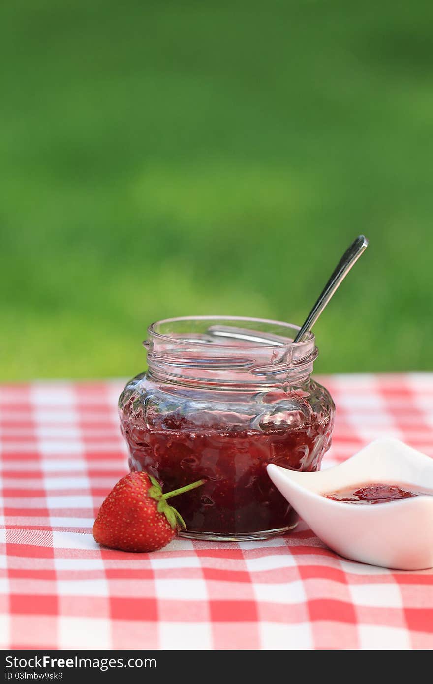 Jar of strawberry jam on the table in the summer garden