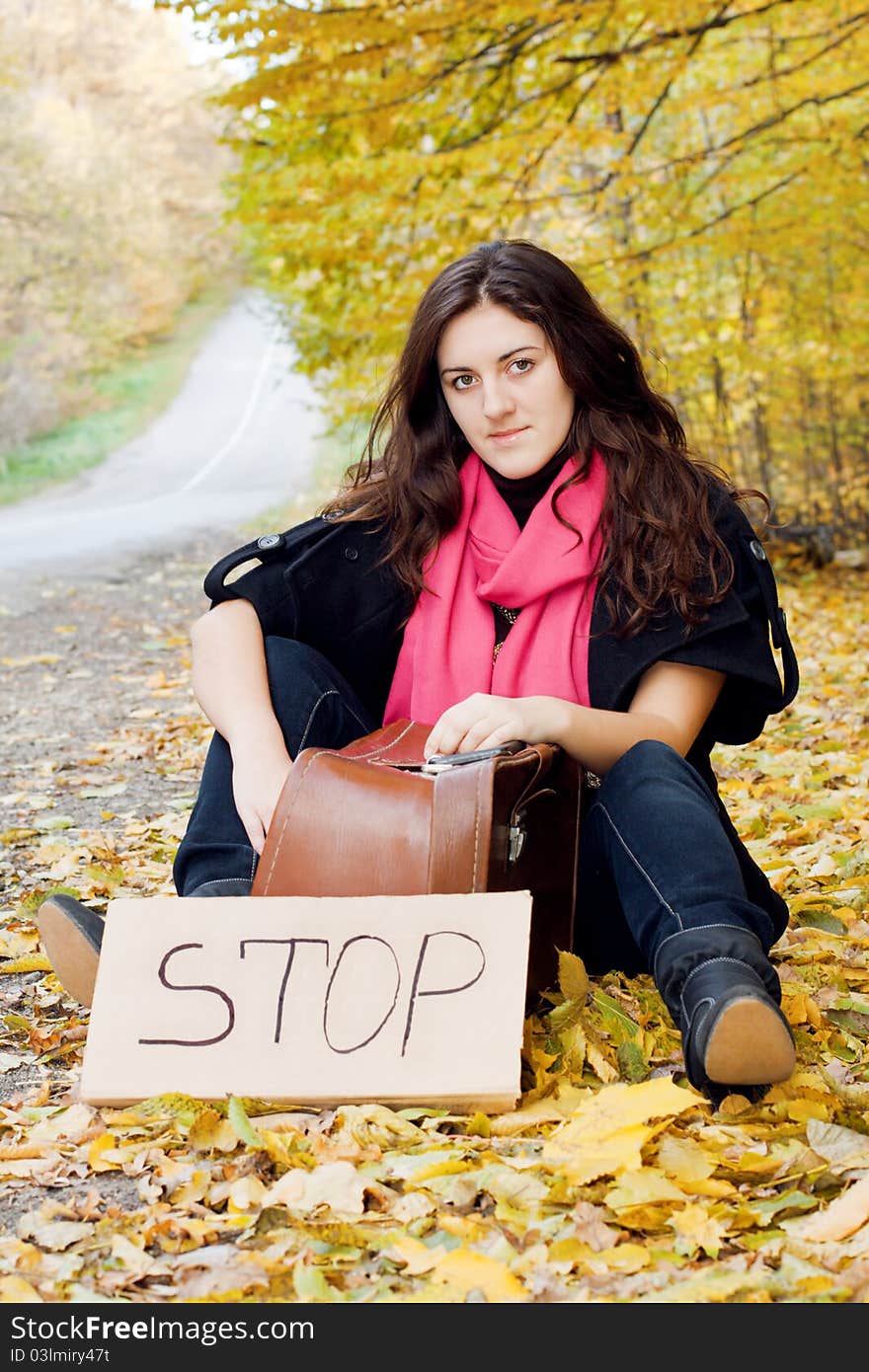 Woman hitchhiking sitting in an autumn bright leaves. Woman hitchhiking sitting in an autumn bright leaves