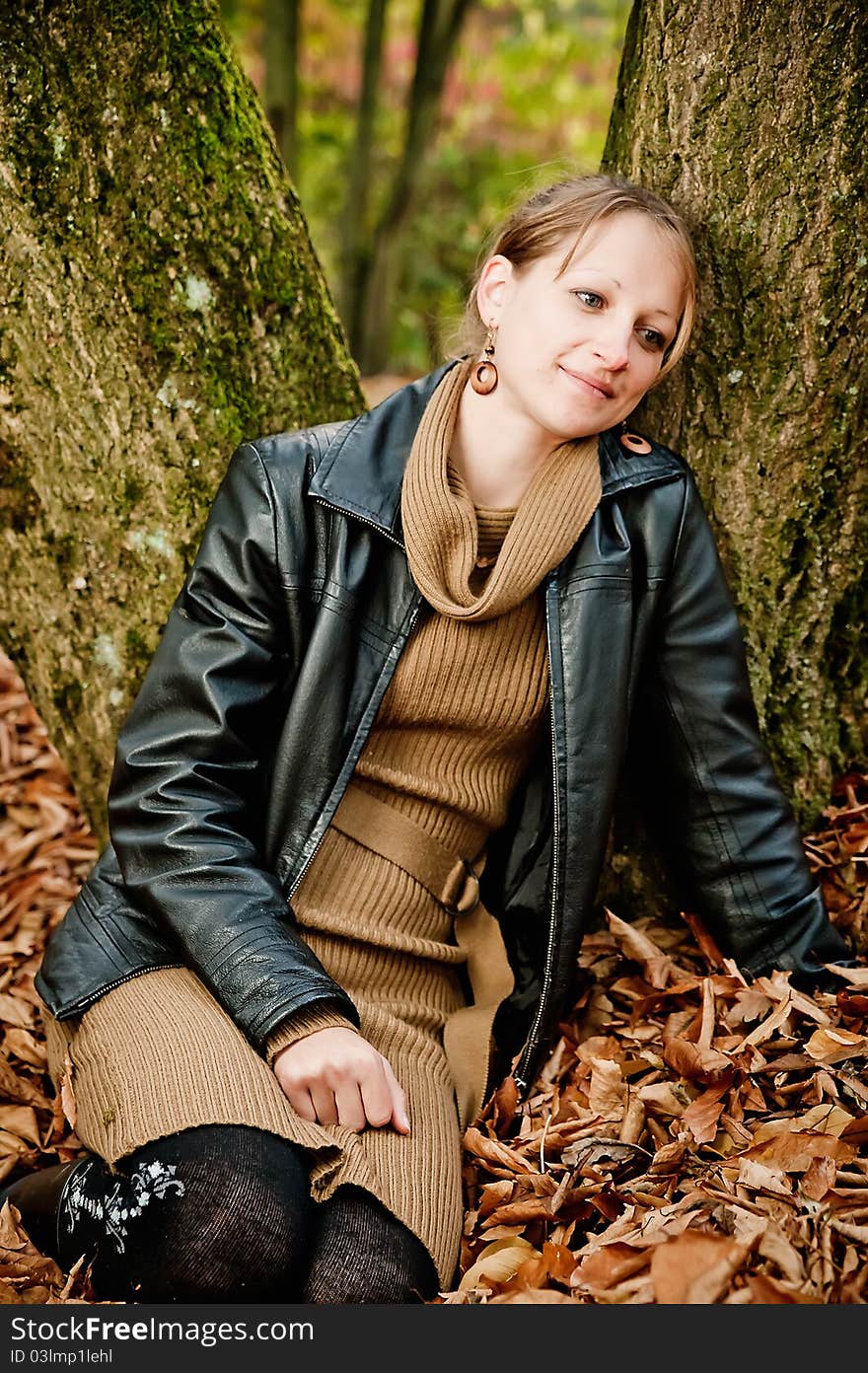 Young woman sitting in autumn leaves and leaning against a tree. Young woman sitting in autumn leaves and leaning against a tree