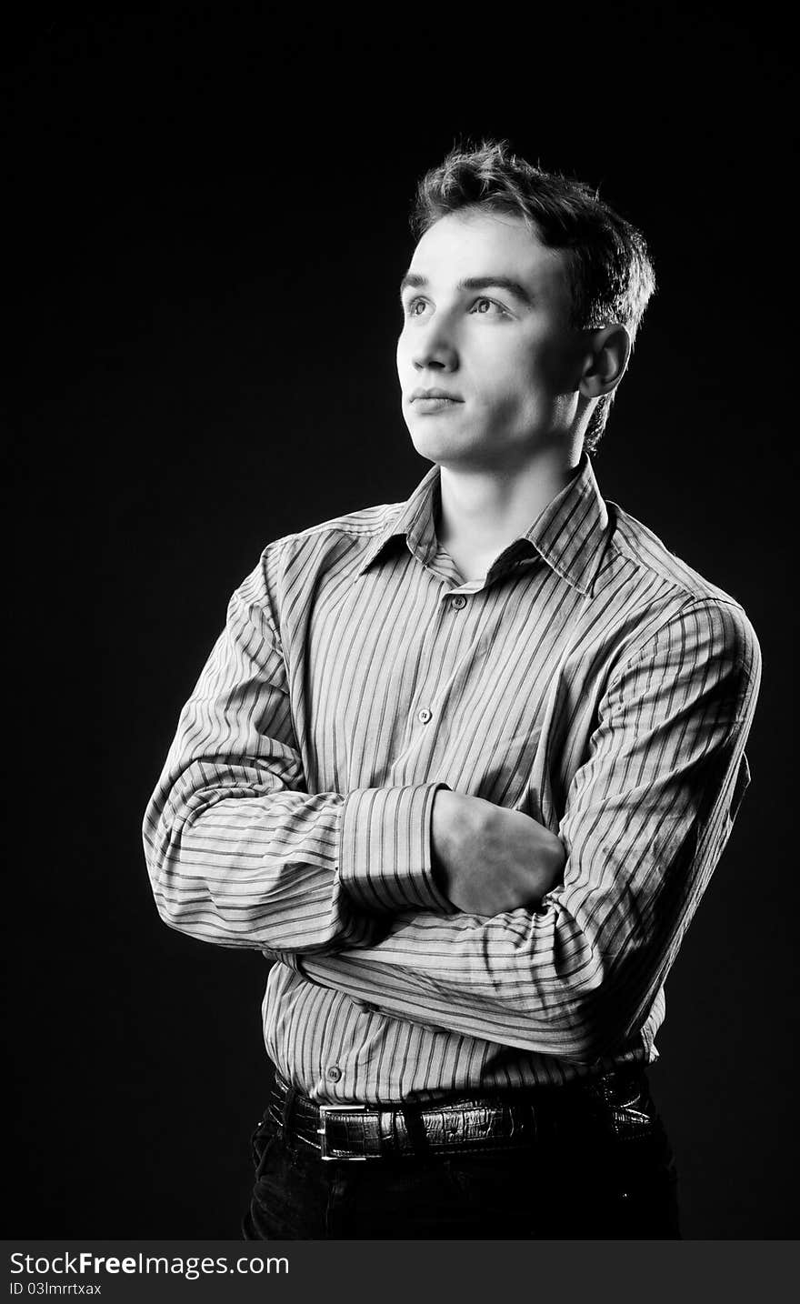 Black and white portrait of a young guy in the studio. Dressed in a shirt and his hands folded on his chest.