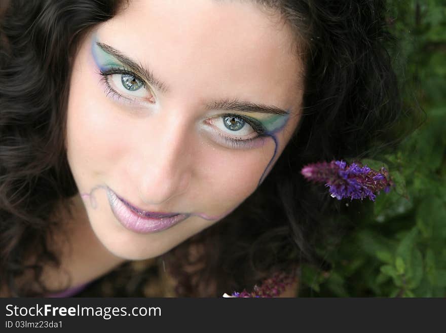 A young woman looking up secretively, a purple flower close to her, a pale rainbow of color on her face.