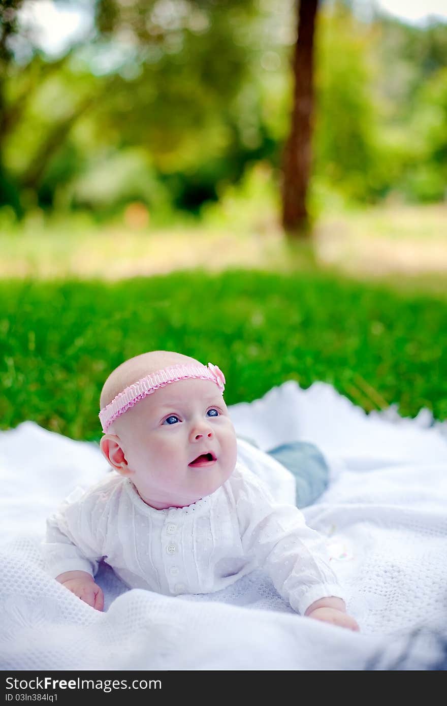 Little baby girl with pink headband lying on her belly on a white counterpane and looking up. Little baby girl with pink headband lying on her belly on a white counterpane and looking up