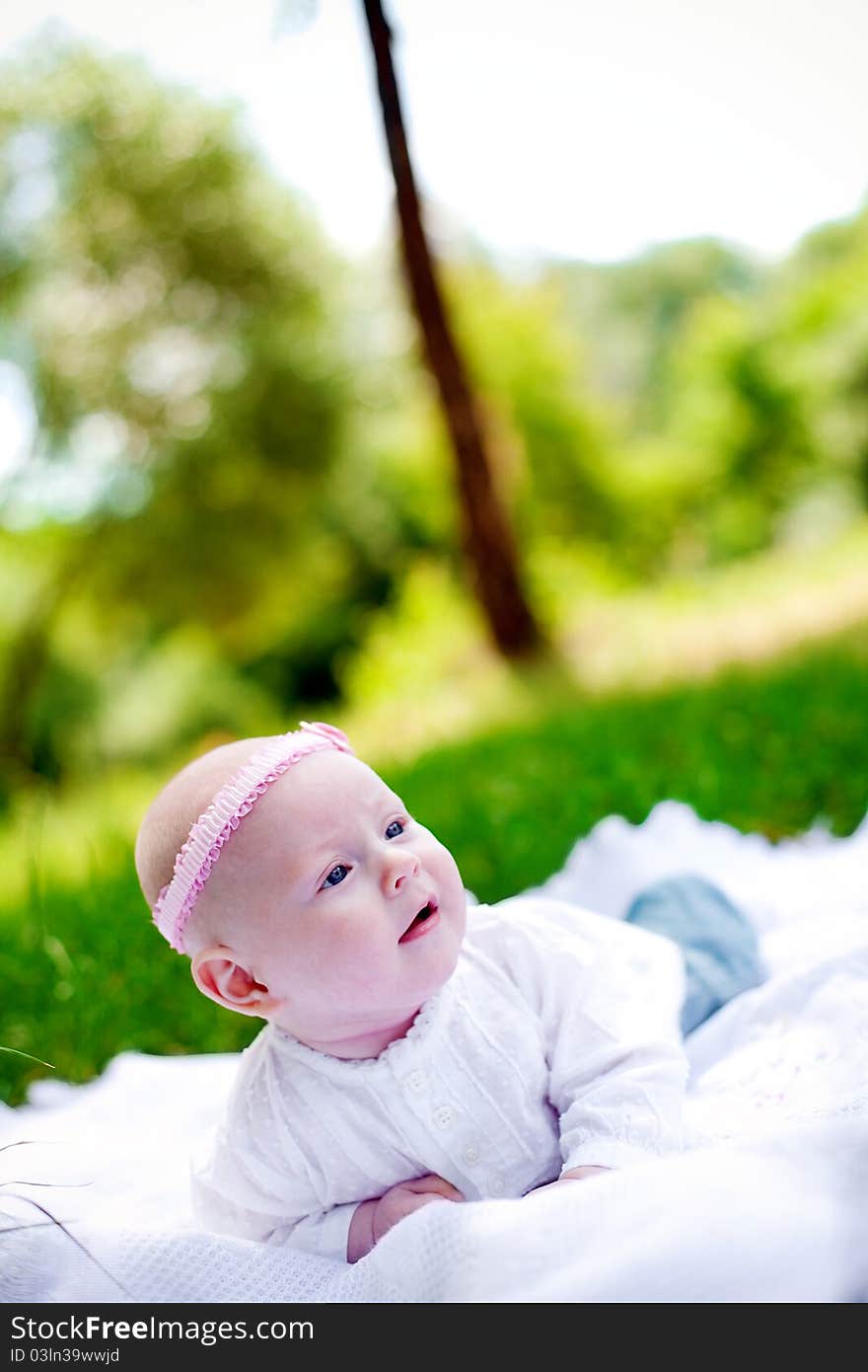 Little baby girl with pink headband lying on her belly on a white counterpane and looking up