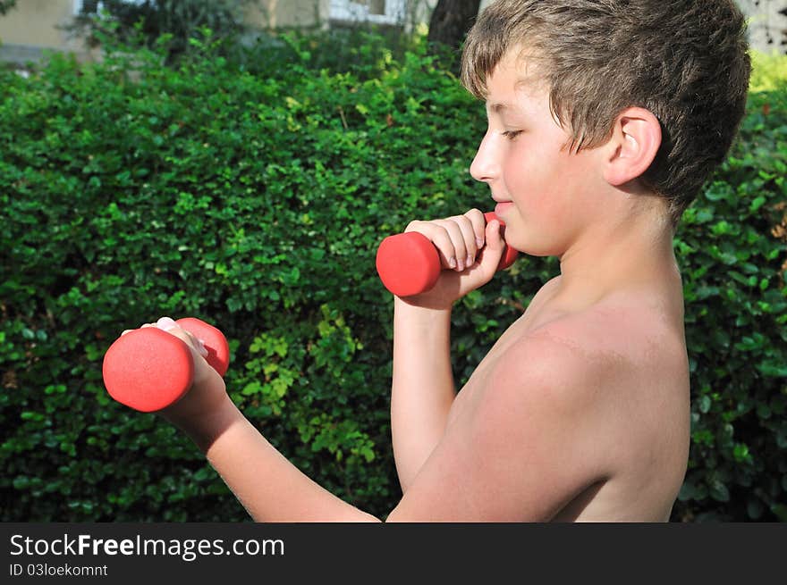 A boy plays sports in the yard of red dumbbell raises. A boy plays sports in the yard of red dumbbell raises